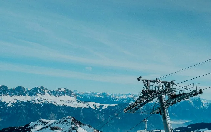 A ski lift tower against snow-covered mountains