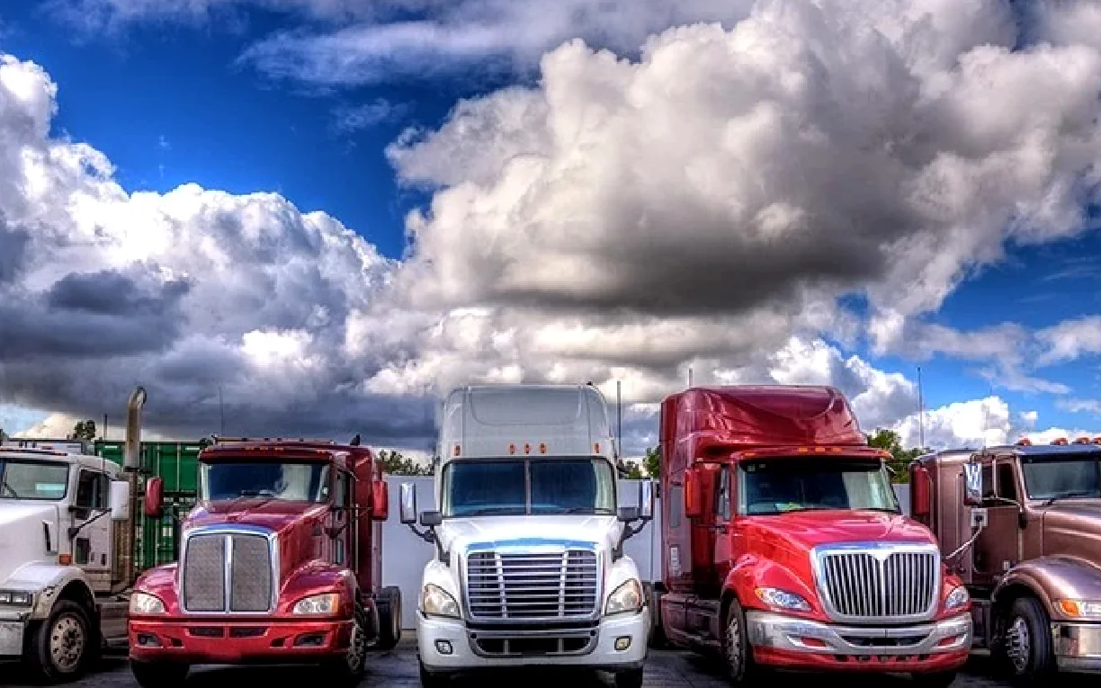 A row of semi-trucks parked nose-out in a yard under a dramatic sky